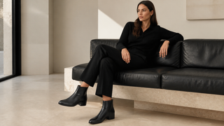 Woman seated on a contemporary black sofa wearing black Aquatalia Ulyssa nappa-leather zip-up boots