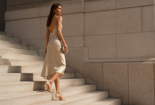 Woman wearing the exact beige patent Miu Miu ankle-strap sandal on modern Italian stone stairs