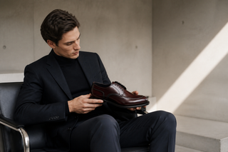 Man examining the exact Franceschetti burgundy-and-black split-toe derby in a modern Italian interior