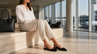 Woman seated in a contemporary airport lounge wearing black Bruno Magli Bella leather slingback flats