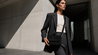 Model carrying an Aquatalia Aria black suede crossbody bag against modern Milan architecture
