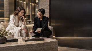 Two women comparing material swatches in a modern Milan luxury retail consultation space.