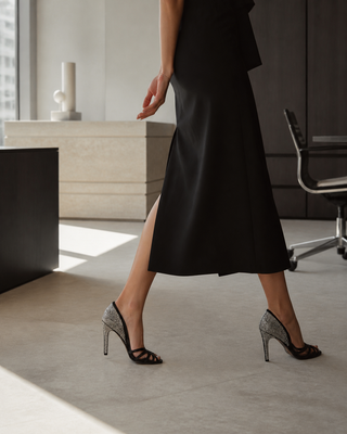 Woman wearing black crystal-embellished Christian Dior peep-toe stiletto sandals in a contemporary Milan office