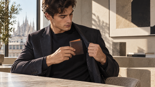 Young professional holding a dark brown pebbled leather wallet in a modern Milan design office.