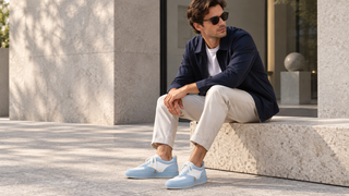 Man wearing pale blue and white suede-and-leather sneakers while seated outside a modern Milan design studio.