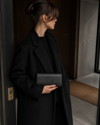 Woman holding the black Gucci Soho pebbled-leather flap wallet in a modern Milan apartment entryway