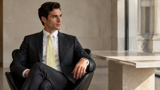 Man in a white dress shirt and charcoal suit wearing a pale lime silk tie in a modern Milan office