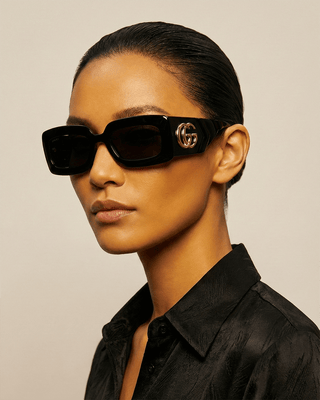 Model wearing Gucci women's sunglasses with dark lenses and iconic logo on the side, featuring a stylish and modern design.